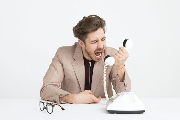 man in tan suit holding a landline phone yelling into it